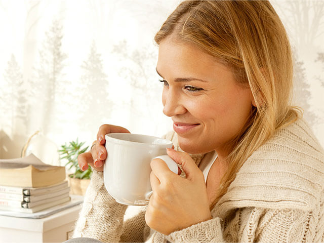 blond kvinde sidder med en kop te og smiler